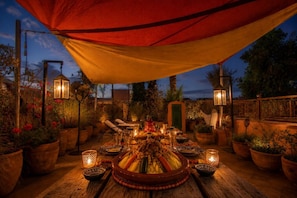 An outdoor dining area with a table set for a meal, surrounded by potted plants and illuminated by lanterns. - Riad Dar Al Barakaa - Exclusive- Breakfast (Marrakech)