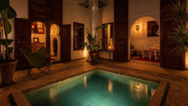 A pool area with wooden doors, potted plants, and a chair. - Riad Dar Al Barakaa - Exclusive- Breakfast (Marrakech)