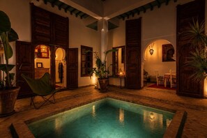 A pool area with wooden doors, potted plants, and a chair. - Riad Dar Al Barakaa - Exclusive- Breakfast (Marrakech)