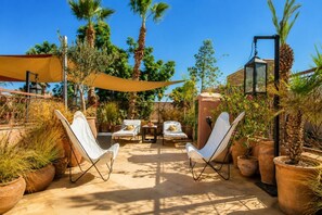 An outdoor patio with two white lounge chairs, a table, and a yellow canopy.