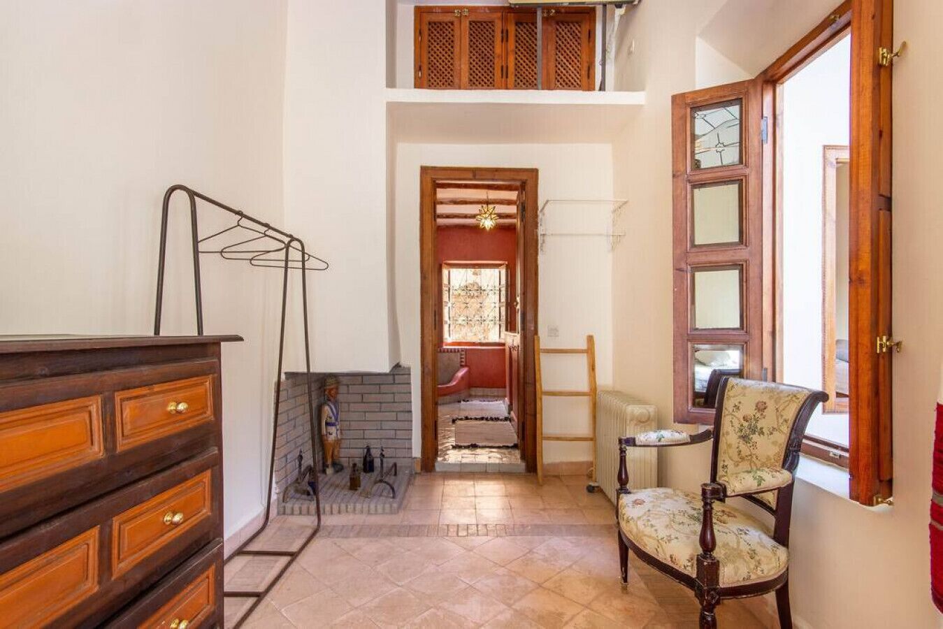 A compact room with a wooden dresser, a chair, a radiator, and a staircase leading to an upper level.