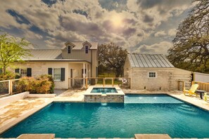 A swimming pool with a stone border, a wooden deck, and a stone building with a metal roof. - Private Ranch Suite-Bar-GameRoom (Fredericksburg)
