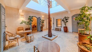 Un pati interior ampli i espaiós, amb un sostre elevat, una palmera al centre, mobles de vimet i plantes en testos.