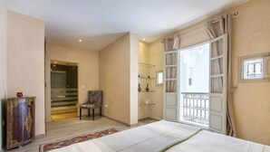A bedroom with a bed, a chair, a wardrobe, a balcony with a railing, and a staircase leading to another room. - Riad Princesses des Sables-Jaccuzzi-Breakfast (Marrakesh)