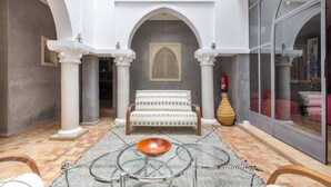 A spacious indoor area with a patterned sofa, a glass table, and a decorative bowl. - Riad Princesses des Sables-Jaccuzzi-Breakfast (Marrakesh)