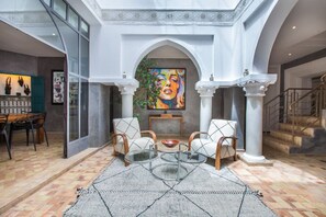 A spacious interior with a dining area, a seating area with a glass coffee table, and a staircase. - Riad Princesses des Sables-Jaccuzzi-Breakfast (Marrakesh)