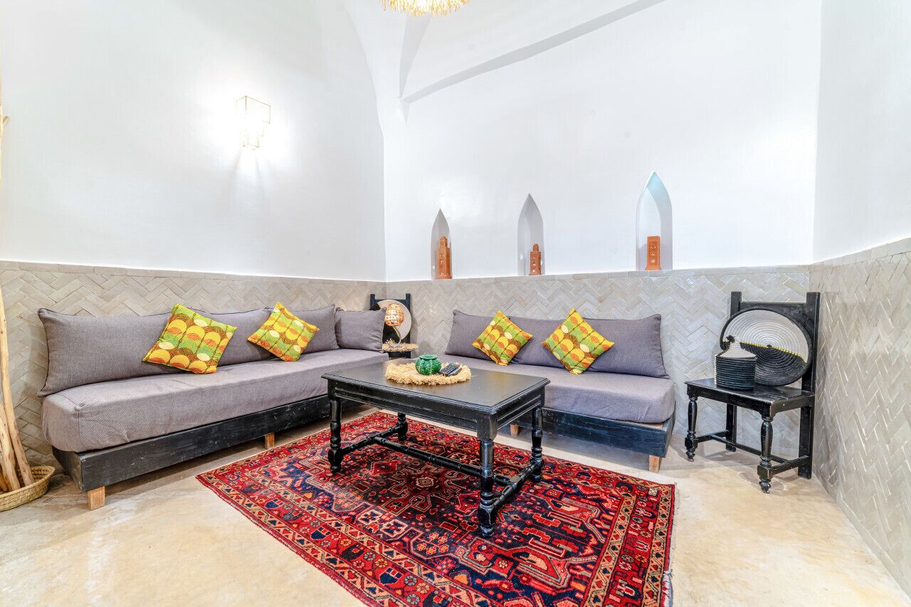 Una sala de estar moderna con un sofá gris, cojines coloridos, una mesa de centro negra y una alfombra roja con estampado.