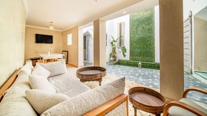 A spacious living area with a sofa, coffee table, and chairs, a dining table, and a view of a green garden through large windows. - Riad Itri (إتري) Exclusif - Marrocan Breakfast (Marrakesh)