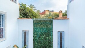 A courtyard with a patterned green screen, two doors, and a view of buildings in the background. - Riad Itri (إتري) Exclusif - Marrocan Breakfast (Marrakesh)