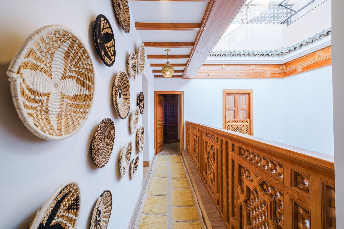 A hallway with woven wall art, wooden railings, and a tiled floor.