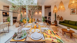 A spacious living area with a dining table set for a meal, surrounded by comfortable seating and decorative plants. - Riad Ouladi -Exclusif - 5mn Jemaa El Fnaa -Pool (Marrakesh)