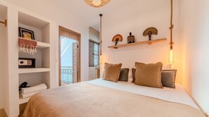 A bedroom with a large bed, a shelf with decorative items, a hanging light, and a view of the outside balcony. - Riad Ouladi -Exclusif - 5mn Jemaa El Fnaa -Pool (Marrakesh)