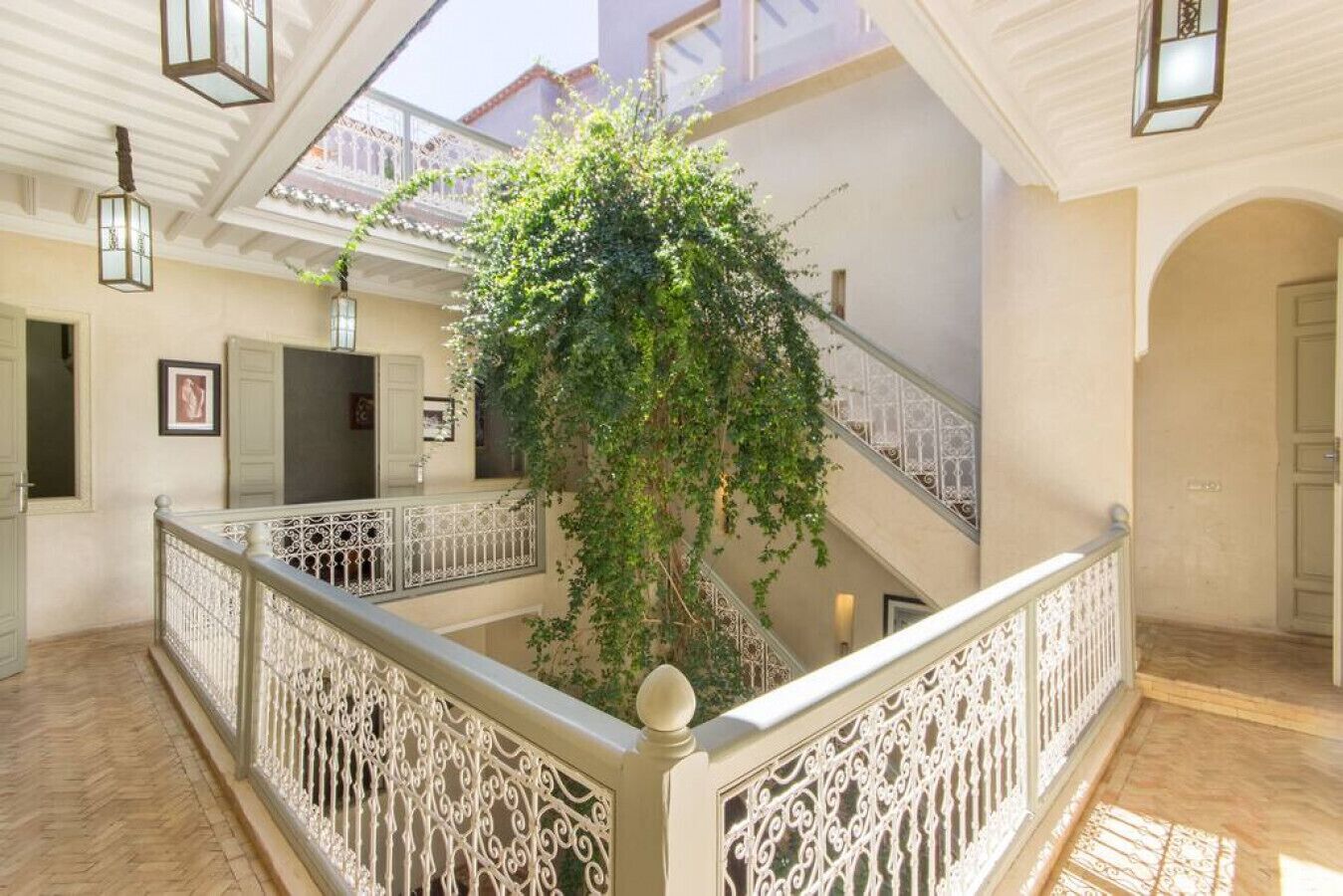 Un vaste atrium agrémenté d’une plante suspendue au centre, de rampes décoratives et d’un escalier doté d’une balustrade blanche.