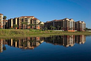 A hotel with multiple buildings, a calm water body in front, and palm trees. - Four Bedroom Condo WestGate Lakes Resort & Spa Universal Studios & SeaWorld (Orlando)