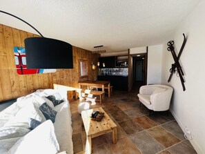 A cozy room with a bed, a wooden coffee table, a white armchair, and a dining area with a table and chairs.