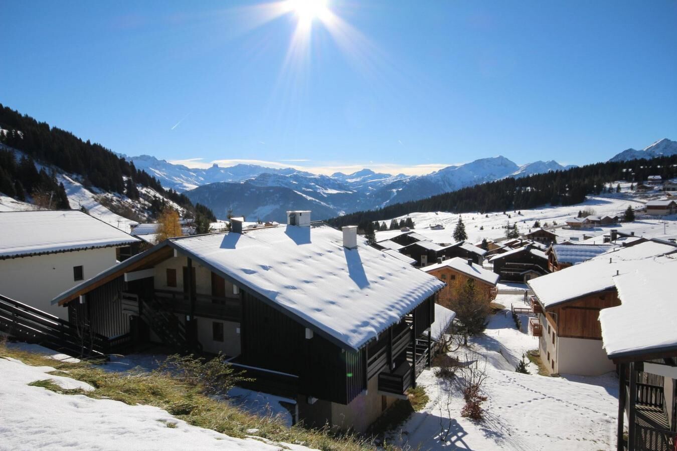 A snow-covered village with traditional wooden houses, a clear sky, and mountains in the background.