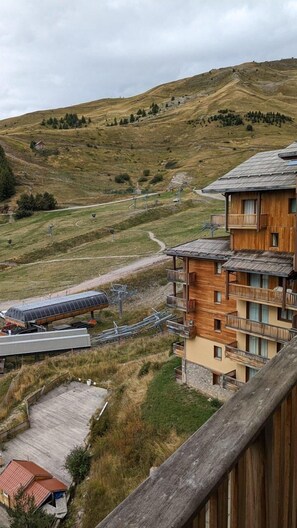 Un bâtiment en bois à plusieurs étages, doté de balcons, qui se dresse sur un paysage vallonné, avec un télésiège visible au loin.