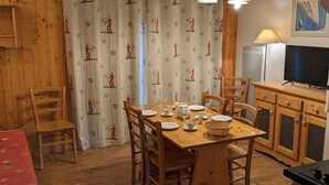 Un tavolo da pranzo in legno apparecchiato con piatti, bicchieri e un cesto. Sedie circondano il tavolo, e una televisione è montata a parete.