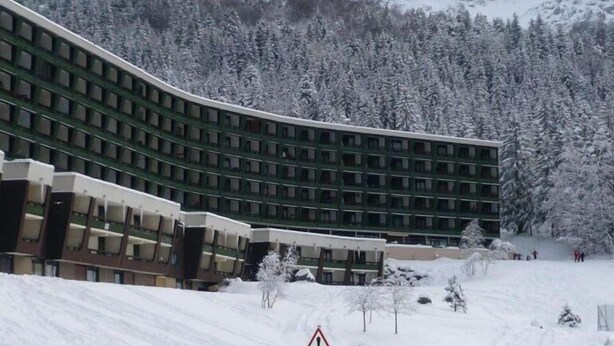 Un hotel de varios pisos con fachada curva, rodeado de árboles nevados y montañas.