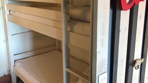 Una cama litera con estructura metálica y un colchón. Hay una puerta con un letrero rojo que dice "Cu".