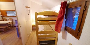 A bunk bed with a red curtain, a wooden desk, and a window with a view of buildings. - 20m from ski slopes, 5th floor, balcony, tv, ski locker, 24m², Tignes (Tignes)