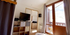 Una stanza con televisione su un mobile in legno, una finestra che si affaccia all'esterno e una porta che conduce a un'altra stanza.