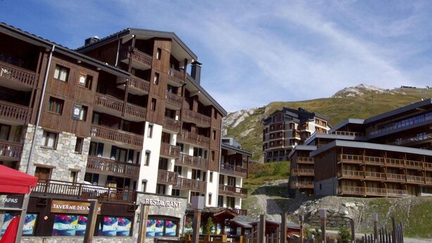Um hotel com vários andares, varandas, um restaurante e vista para uma montanha.