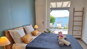 Un dormitorio con cama, almohadas, lámpara y vista al mar, además de una escalera.