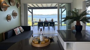 Un salón moderno con sofá, una mesa baja con bebidas y vista al mar a través de amplios ventanales.