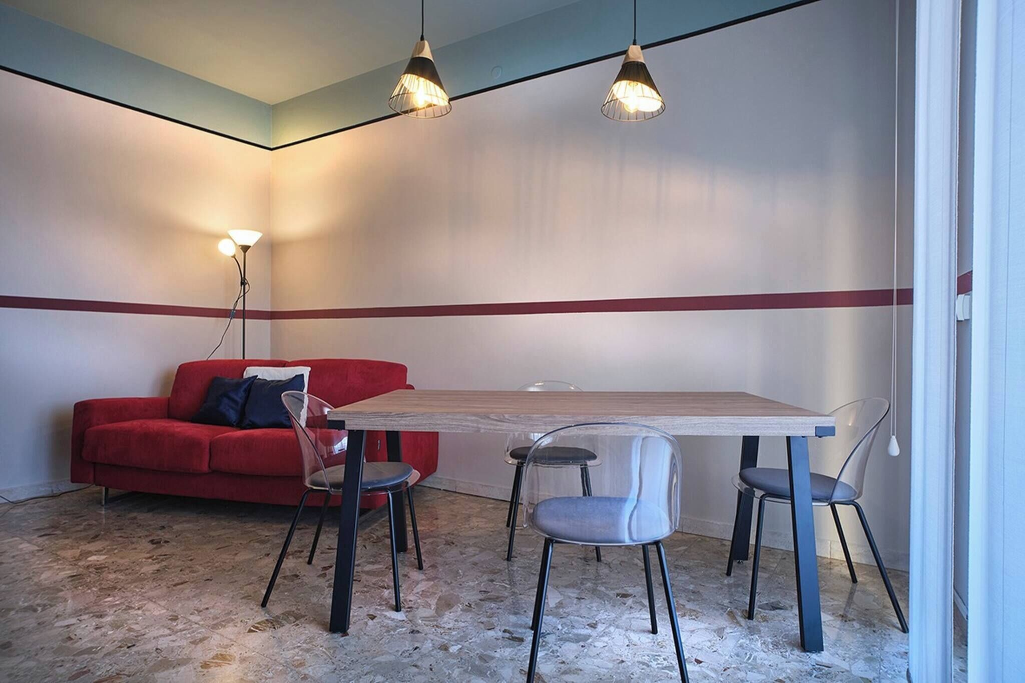 A room with a red sofa, a wooden table, and four chairs. There are three pendant lights above the table.
