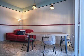 A room with a red sofa, a wooden table, and four chairs. There are three pendant lights above the table.