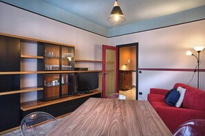 A compact living space with a wooden dining table, a red sofa, a TV, and built-in shelving with glassware.