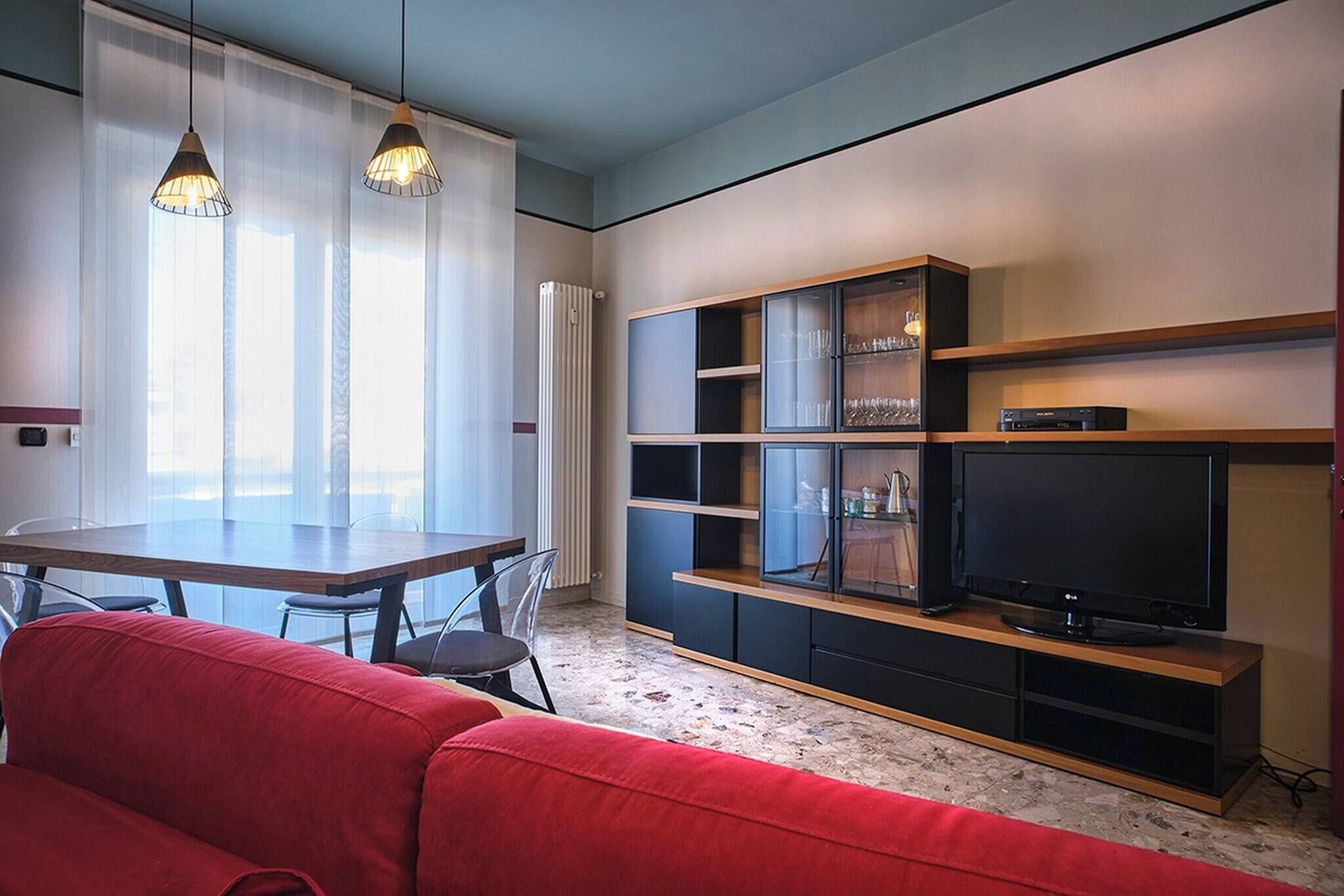 Una sala de estar moderna con un sofá rojo, un televisor sobre un mueble de madera y un comedor con mesa y sillas.