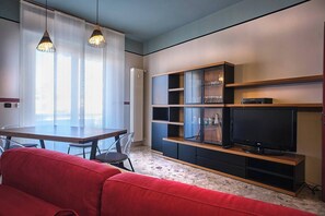 A modern living room with a red sofa, a TV on a wooden stand, and a dining area with a table and chairs.