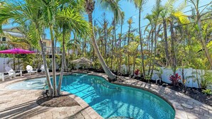 Ein Pool mit geschwungener Form, umgeben von Palmen und einer Pflasterterrasse.