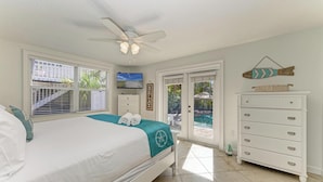 Ein Schlafzimmer mit Bett, Deckenventilator, Fernseher, Kommode und Blick auf einen Pool durch eine Glastür.