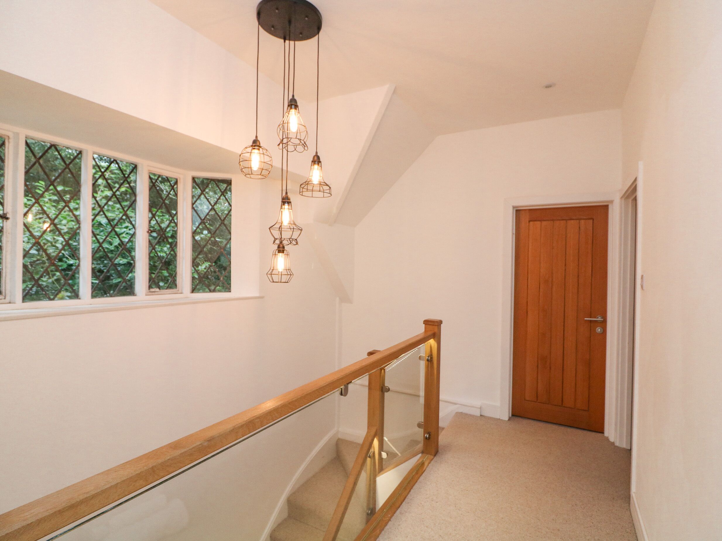 A staircase with a wooden handrail and glass balustrade, leading to a wooden door.