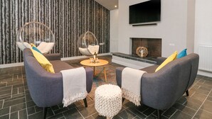 A modern living room with two grey sofas, a round coffee table, and a hanging chair. A fireplace is visible in the background. - Landmark (Salcombe)