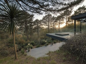 A modern outdoor seating area with a glass railing overlooking a forested landscape. - Landmark (Salcombe)