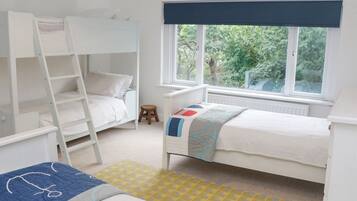A child's bedroom with bunk beds, a small stool, and a window with a view of greenery.