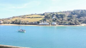 A coastal scene with a sailboat on calm waters, a sandy beach, and houses on a hillside. - Landmark (Salcombe)