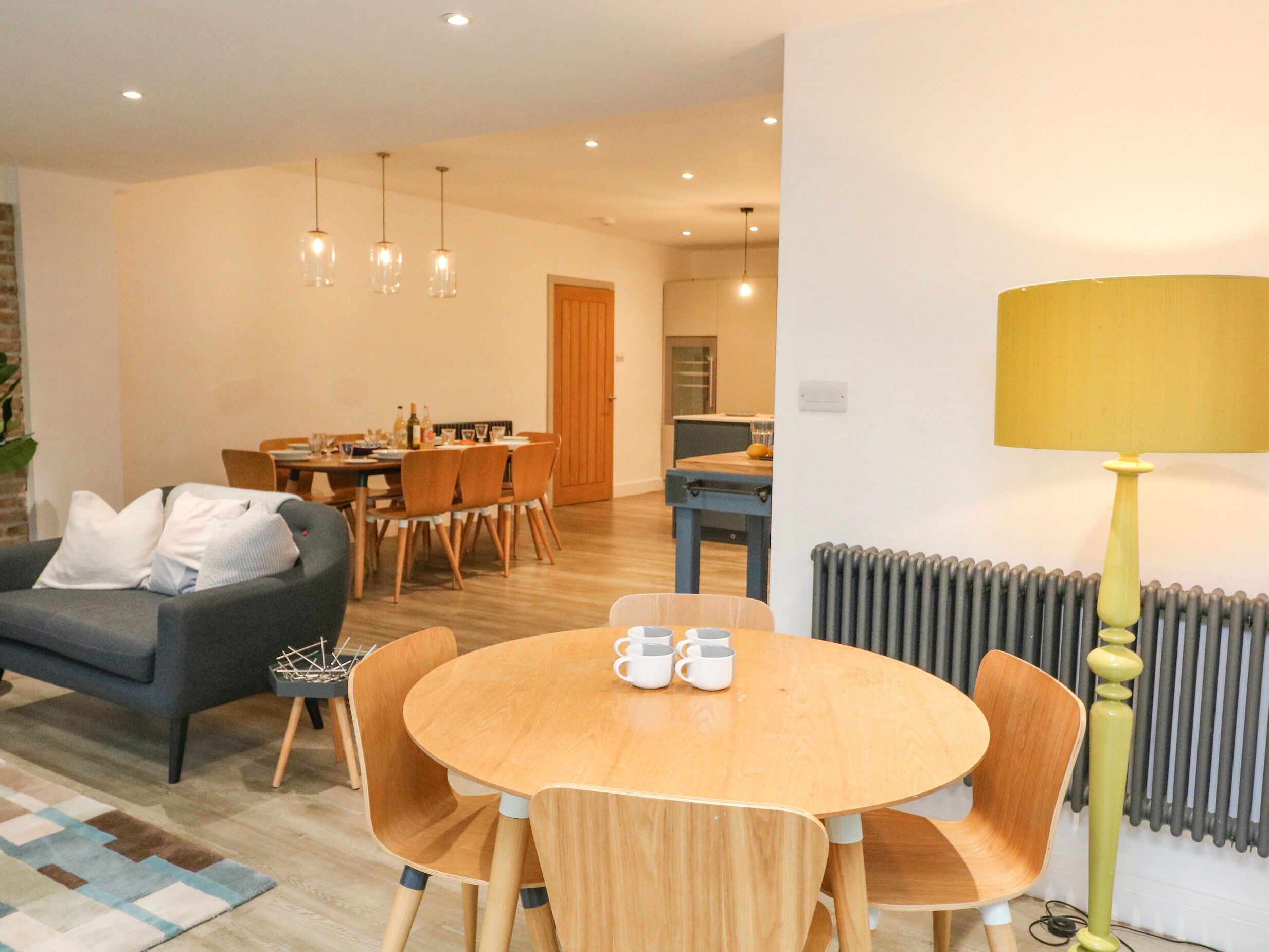 A modern living room with a grey sofa, wooden dining table, and chairs. There is a lamp and a radiator in the room.