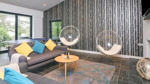 A modern living room with a gray sofa, two hanging chairs, a ping pong table, and a large window. - Landmark (Salcombe)