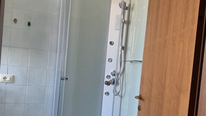 Une cabine de douche fermée par des parois en verre, avec un sol carrelé de blanc, une pomme de douche et un panneau de commande.