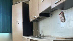 Une cuisine avec des meubles de couleur bois clair, un évier en acier inoxydable et une fenêtre ornée d’un rideau bleu.