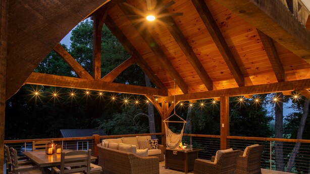 An outdoor deck with wooden beams, a table with chairs, and a hammock.