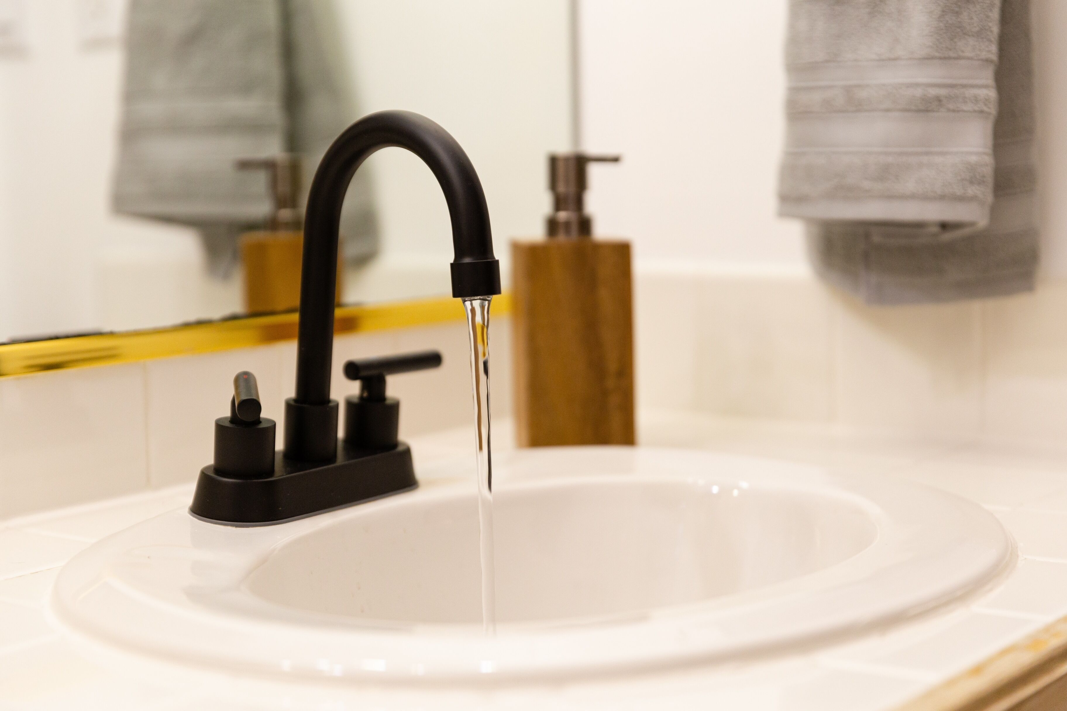 Un lavabo de salle de bain moderne, doté d’un robinet noir et d’un bac en verre transparent.