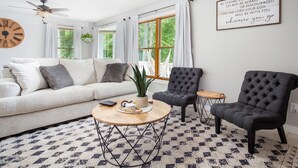 A modern living room with a sofa, two armchairs, a coffee table, and a wall clock.