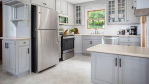 A modern kitchen with white cabinetry, stainless steel appliances, and a large window providing a view of greenery outside.