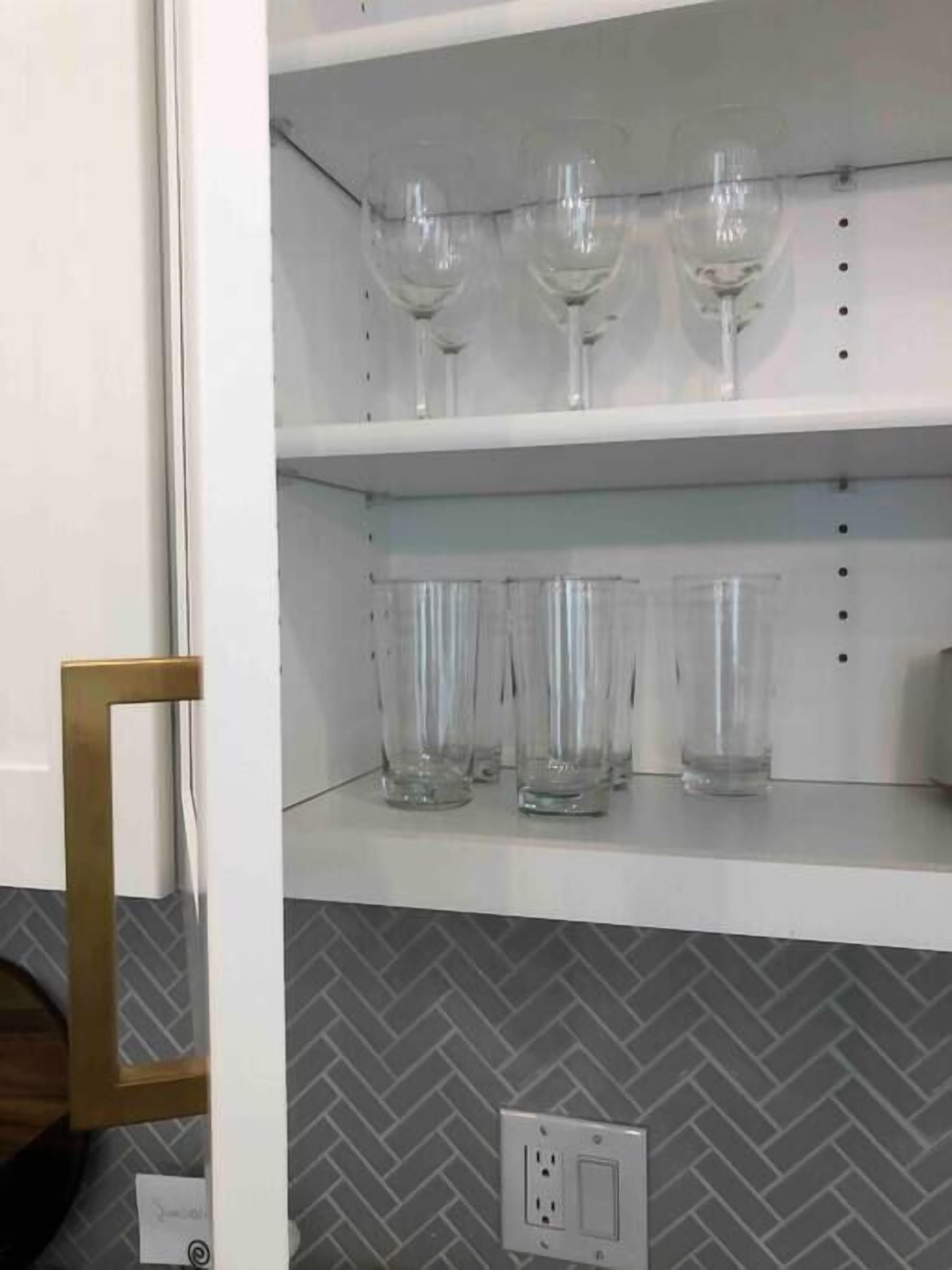 Une pièce avec un mur blanc et un parquet à motifs en chevrons. On y trouve une étagère avec trois verres à vin et une prise électrique sur le mur.